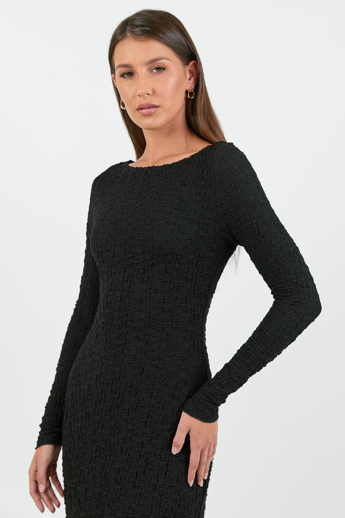 A woman wearing a long-sleeve black textured maxi dress with a fitted silhouette.