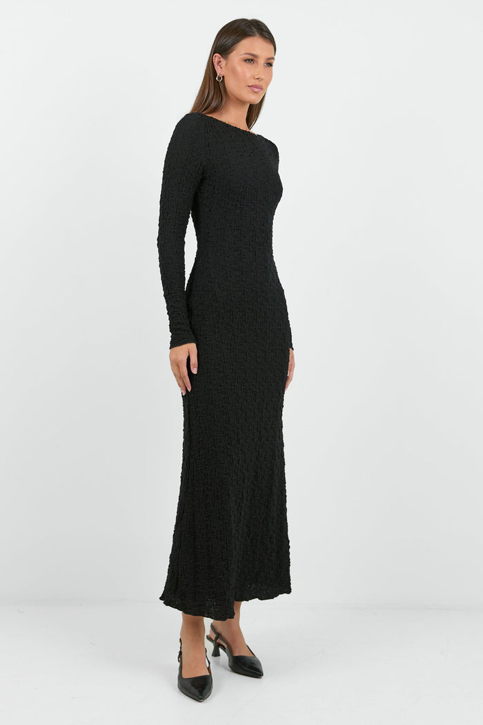 A woman wearing a long-sleeve black textured maxi dress with a fitted silhouette.