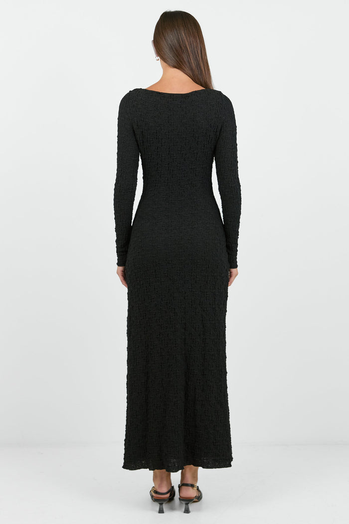 A woman wearing a long-sleeve black textured maxi dress with a fitted silhouette.