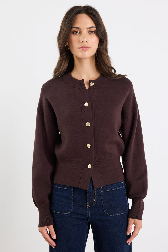 Woman wearing a brown cardigan with gold buttons on a white background