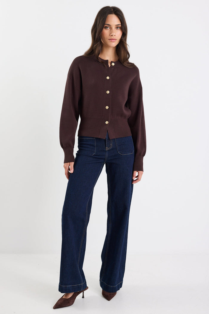Woman wearing a brown cardigan and blue jeans on a white background