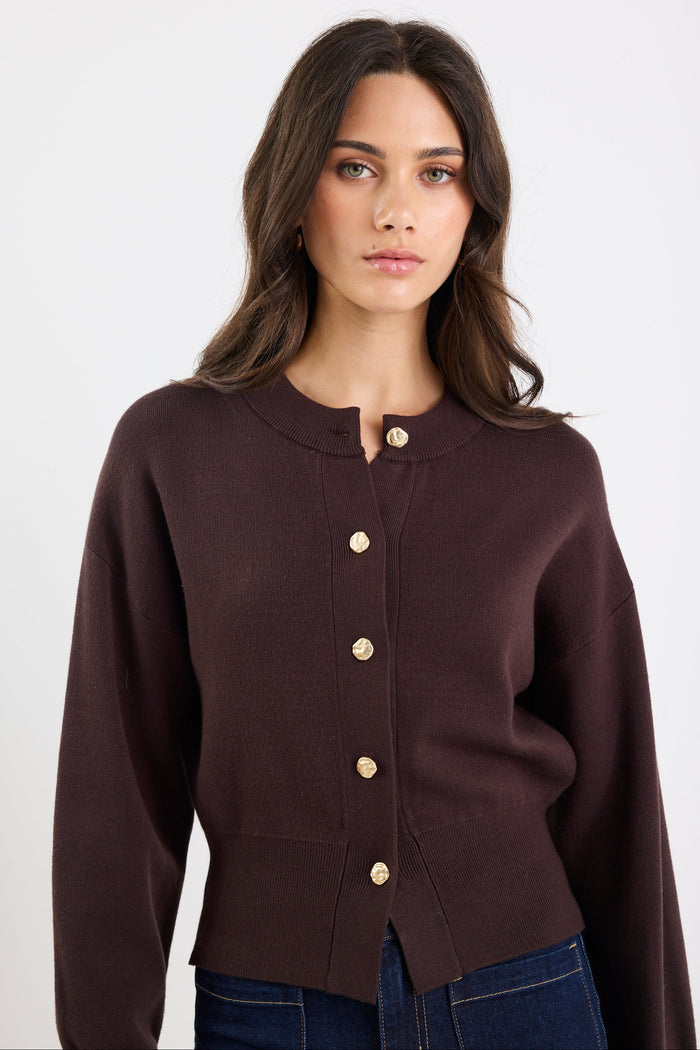 Woman wearing a brown cardigan with gold buttons on a white background