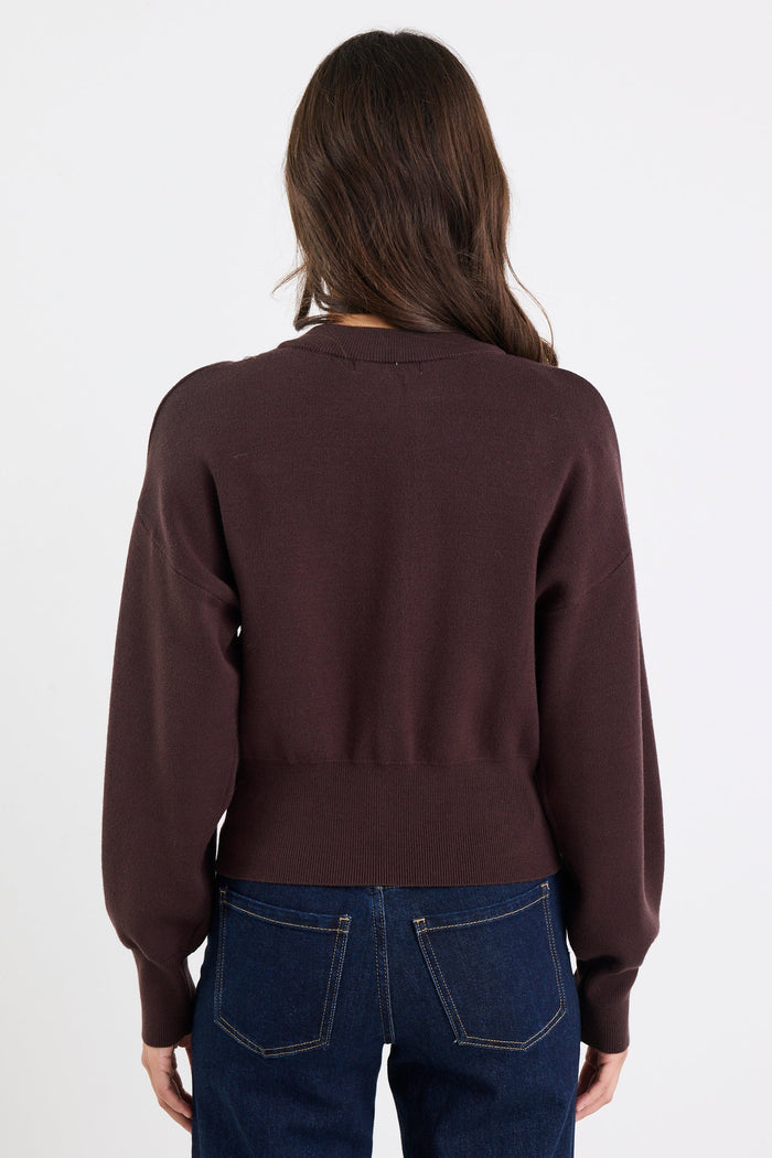 Person wearing a brown sweater and blue jeans on a white background