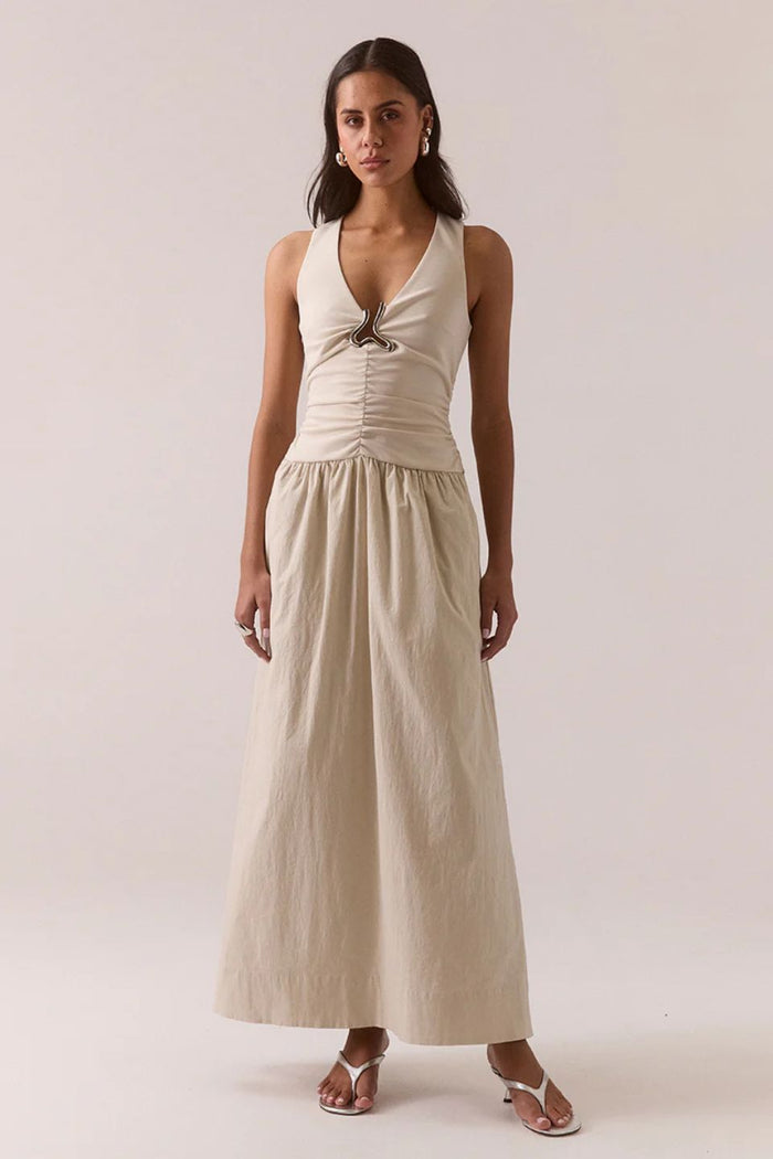 Woman wearing a beige sleeveless dress against a plain background
