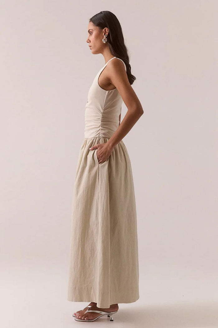 Woman wearing a beige sleeveless dress against a plain background