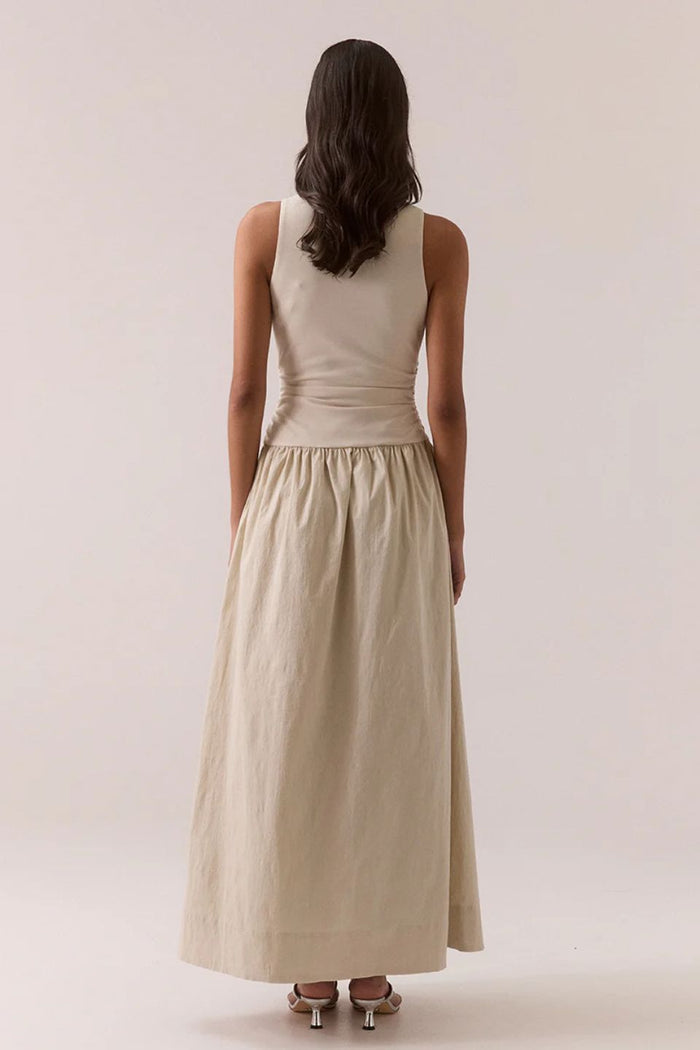 Woman wearing a beige sleeveless dress against a plain background