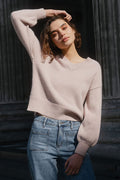 Woman in a light pink sweater and blue jeans standing in front of classical columns.