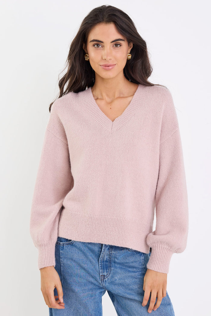 Woman wearing a pink sweater and blue jeans against a white background