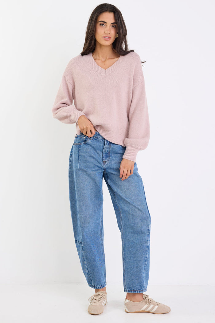 Woman wearing a pink sweater and blue jeans on a white background