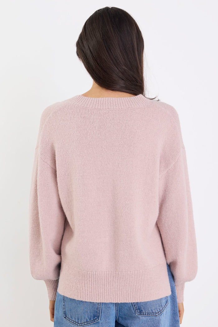 Person wearing a light pink sweater and blue jeans on a white background