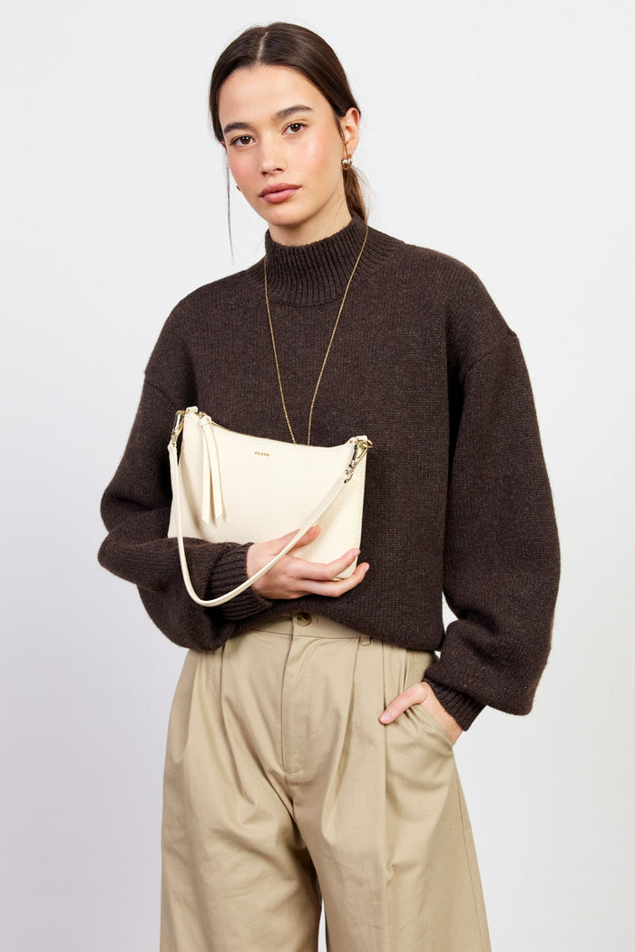 Woman holding a beige handbag against a plain background