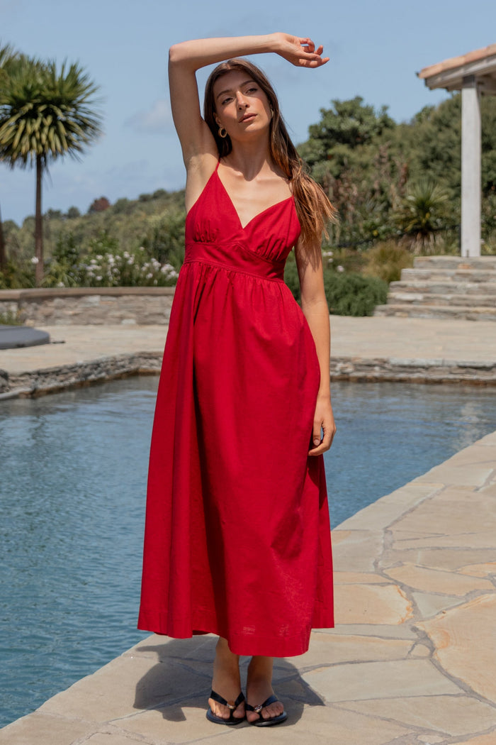 Woman in a red dress standing by a pool with palm trees and a building in the background