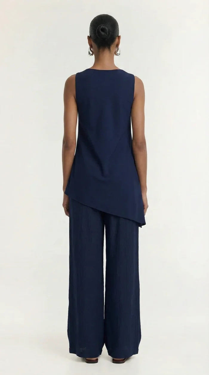 A model viewed from the back wearing a navy blue sleeveless top with an asymmetrical hem and matching wide-leg pants, set against a plain white studio background.