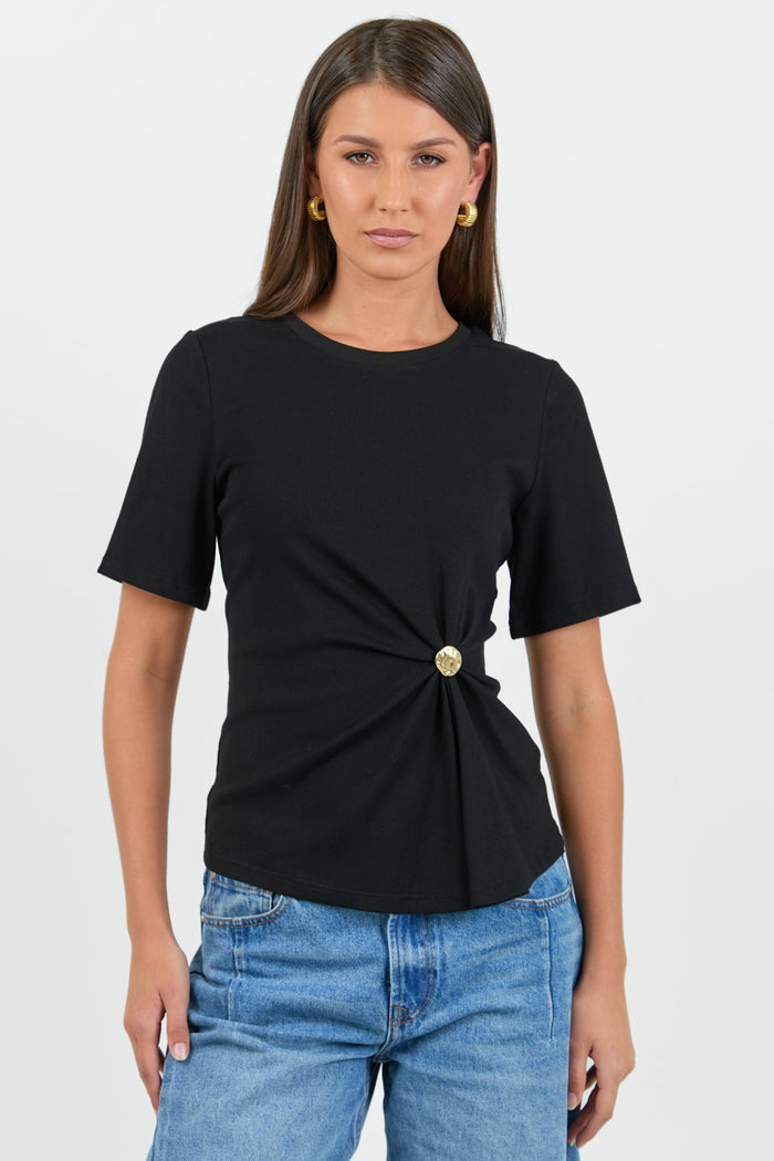 Woman wearing a black top with a gold button and blue jeans on a white background