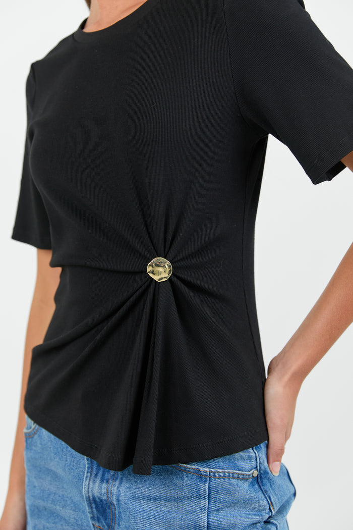 Black top with a gold button detail worn by a person on a white background