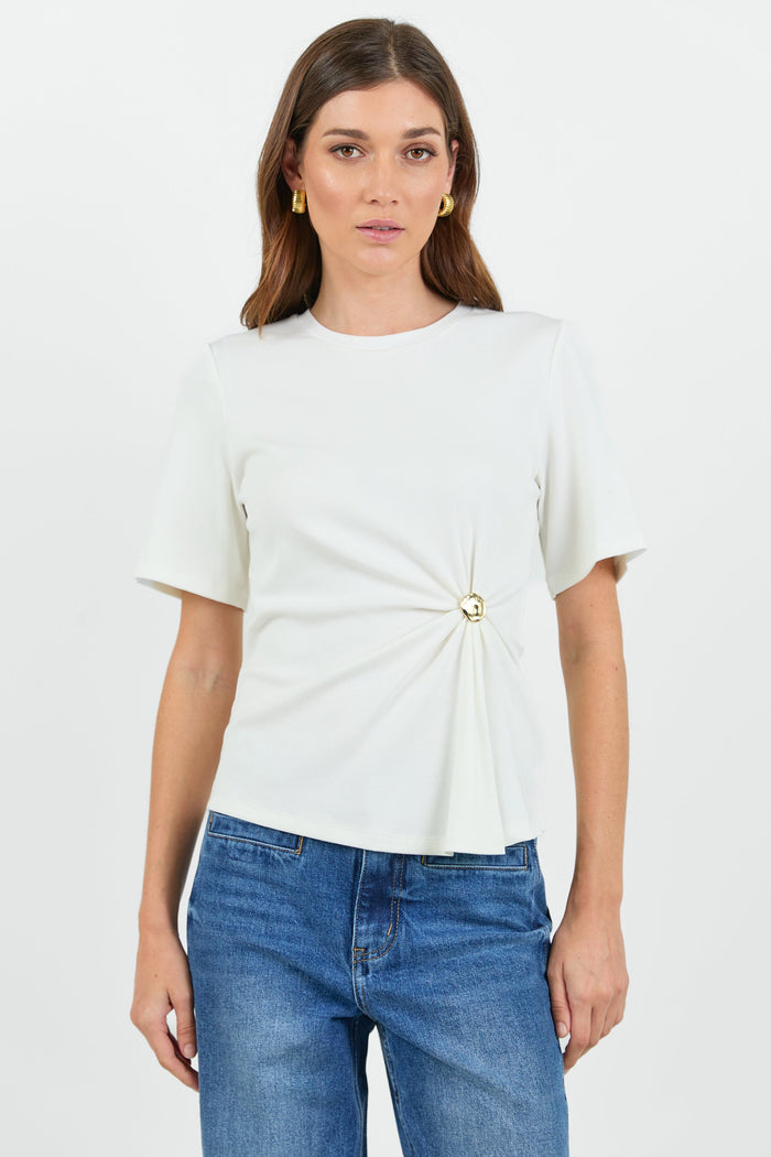Woman wearing a white t-shirt with a twist and clasp detail and blue jeans on a white background