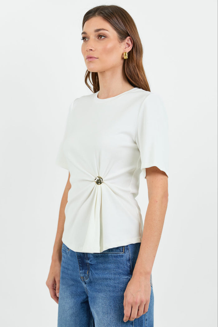 Woman wearing a white t-shirt with a twist and clasp detail and blue jeans on a white background