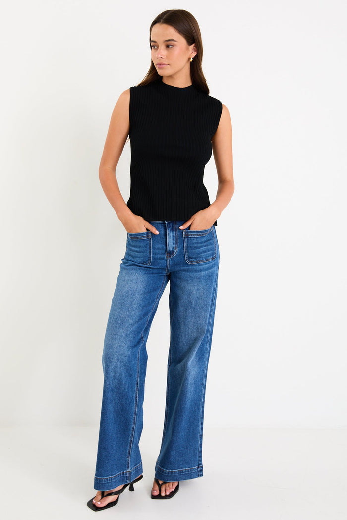 Woman wearing a black sleeveless top and blue jeans on a white background
