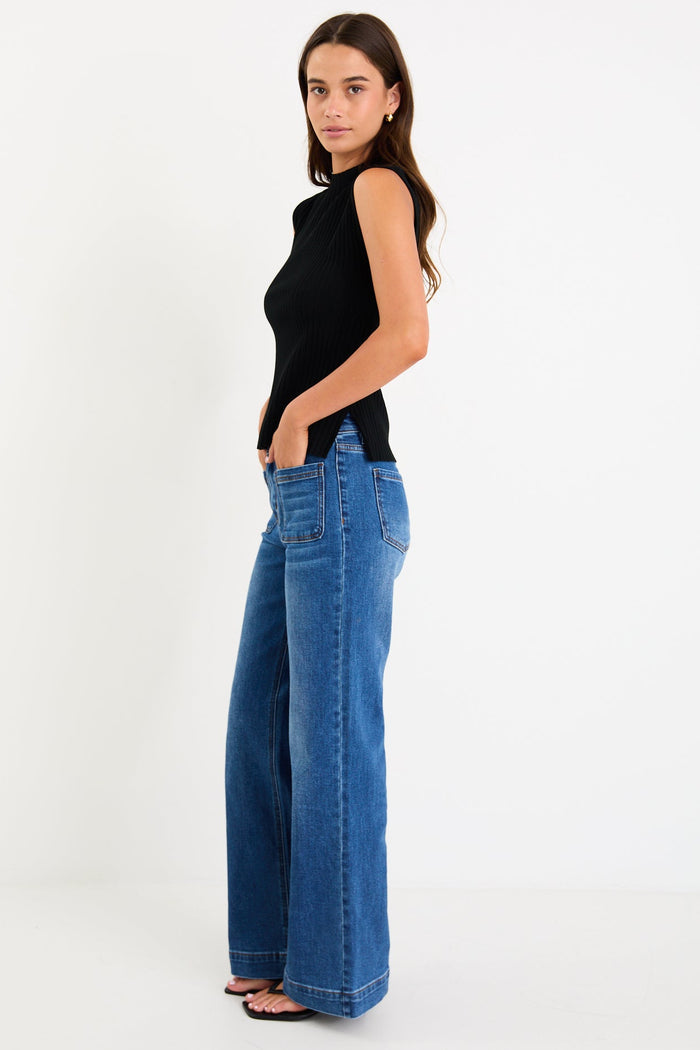 Woman wearing a black sleeveless top and blue jeans on a white background
