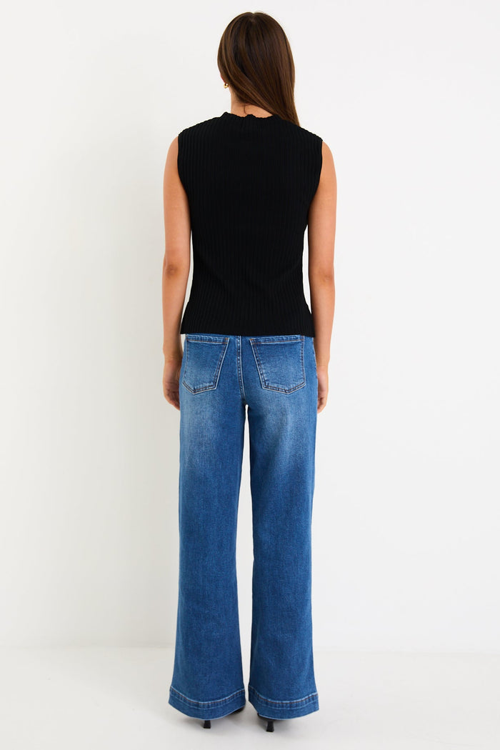 Person wearing a black sleeveless top and blue jeans on a white background