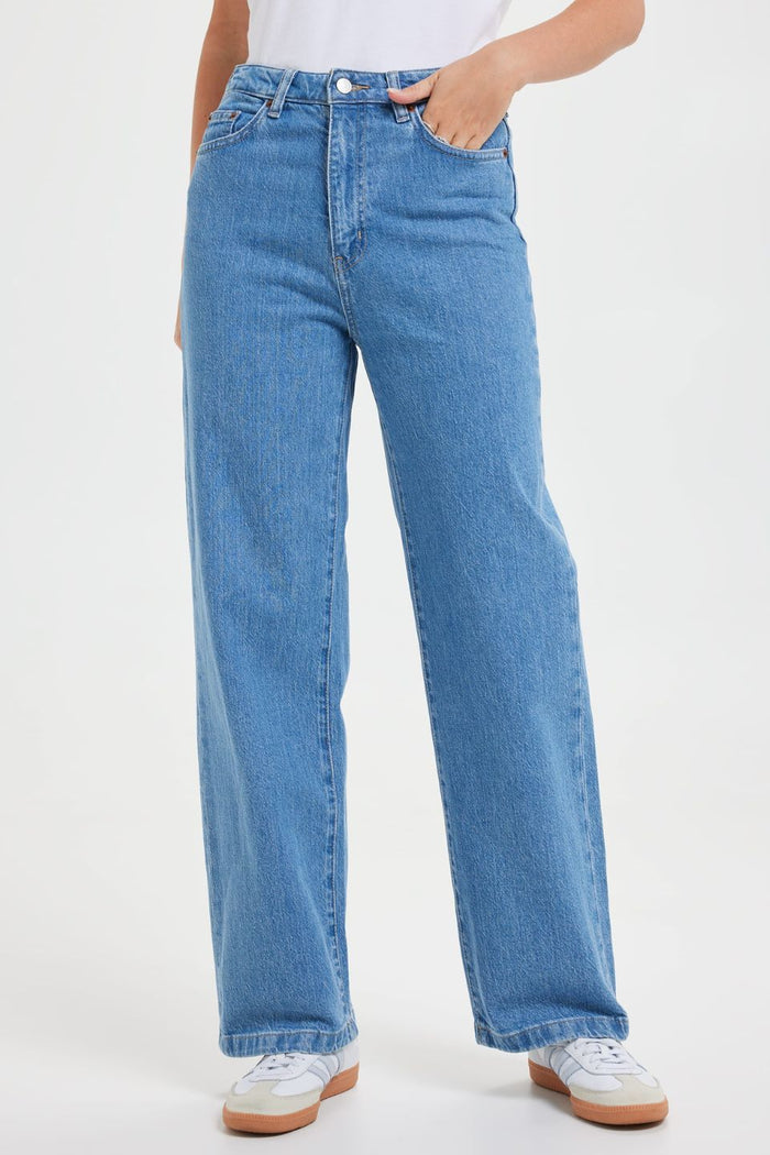 Woman wears high-rise blue wide-leg jeans with a fitted waist and relaxed leg, styled with a white graphic tee and white sneakers. The look is casual, fresh, and flattering.