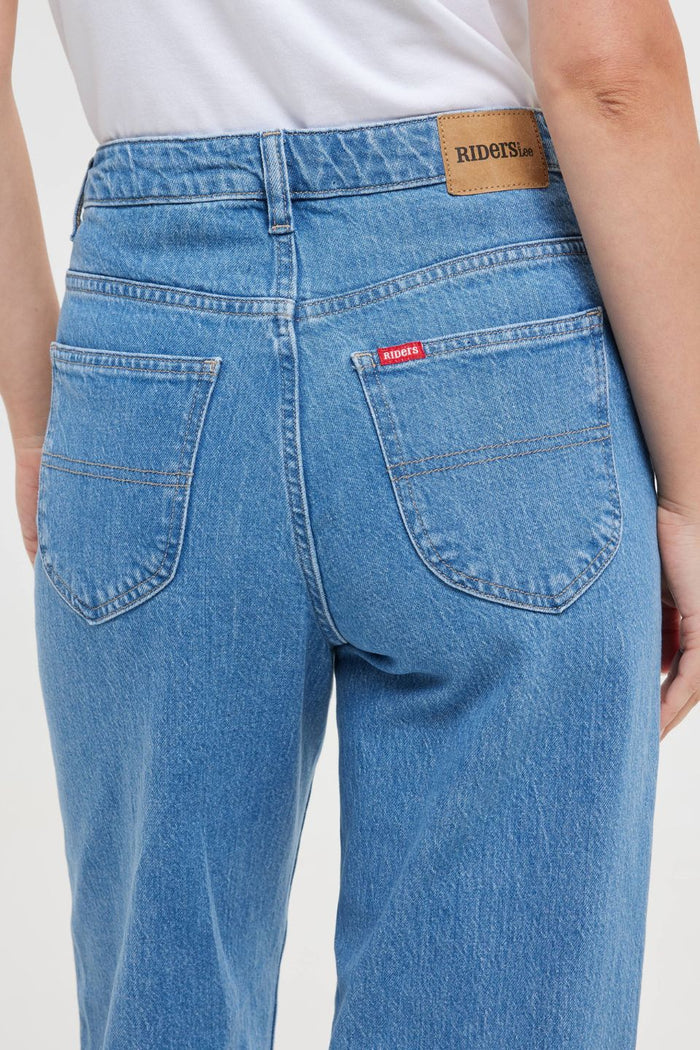 Woman wears high-rise blue wide-leg jeans with a fitted waist and relaxed leg, styled with a white graphic tee and white sneakers. The look is casual, fresh, and flattering.