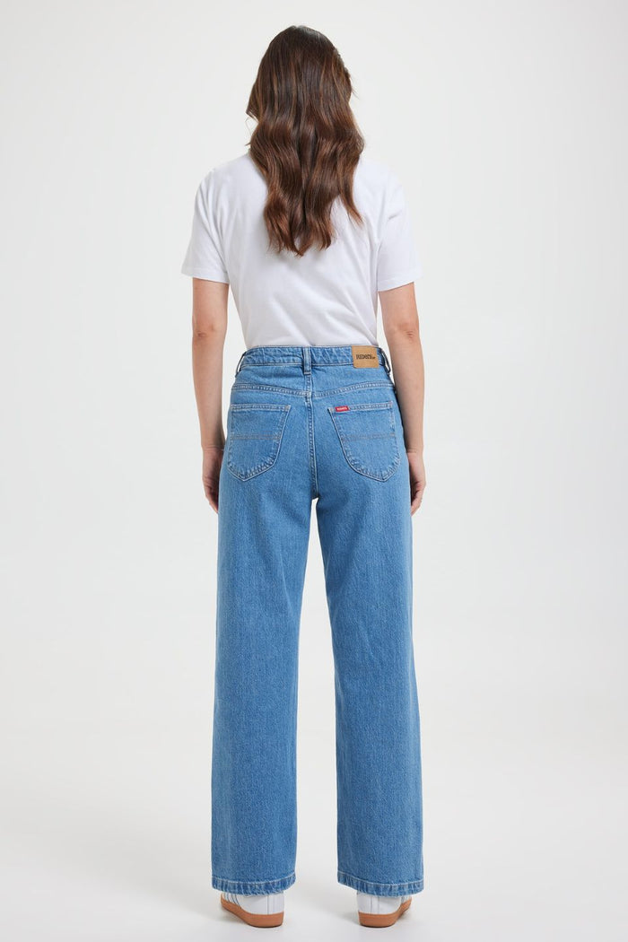 Woman wears high-rise blue wide-leg jeans with a fitted waist and relaxed leg, styled with a white graphic tee and white sneakers. The look is casual, fresh, and flattering.