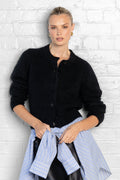 Woman wearing a black cardigan over a blue shirt against a white brick wall