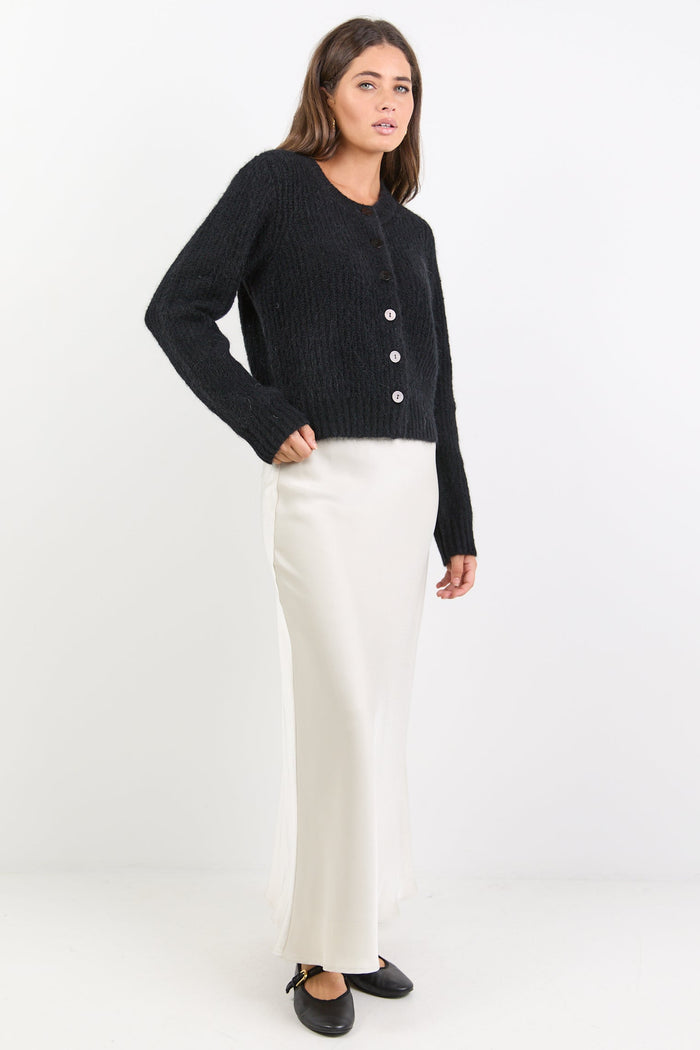 Woman wearing a black cardigan and white skirt on a white background