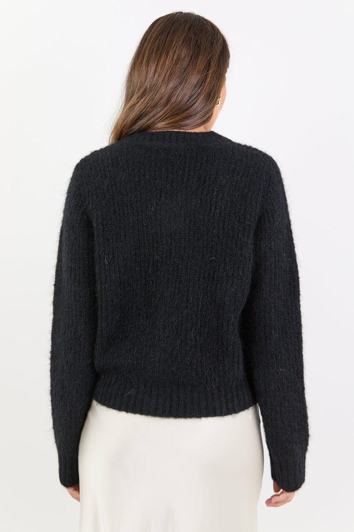 Person wearing a black sweater and white skirt on a plain background