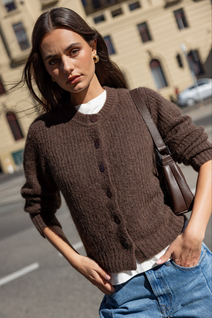 Woman wearing a brown knitted cardigan and blue jeans on a street.
