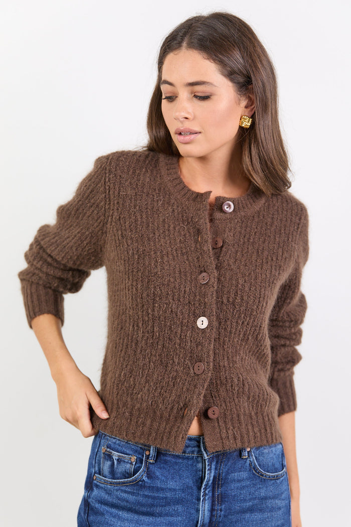 Woman wearing a brown knitted cardigan and blue jeans on a white background