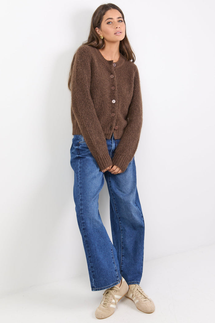 Woman wearing a brown cardigan and blue jeans against a white background