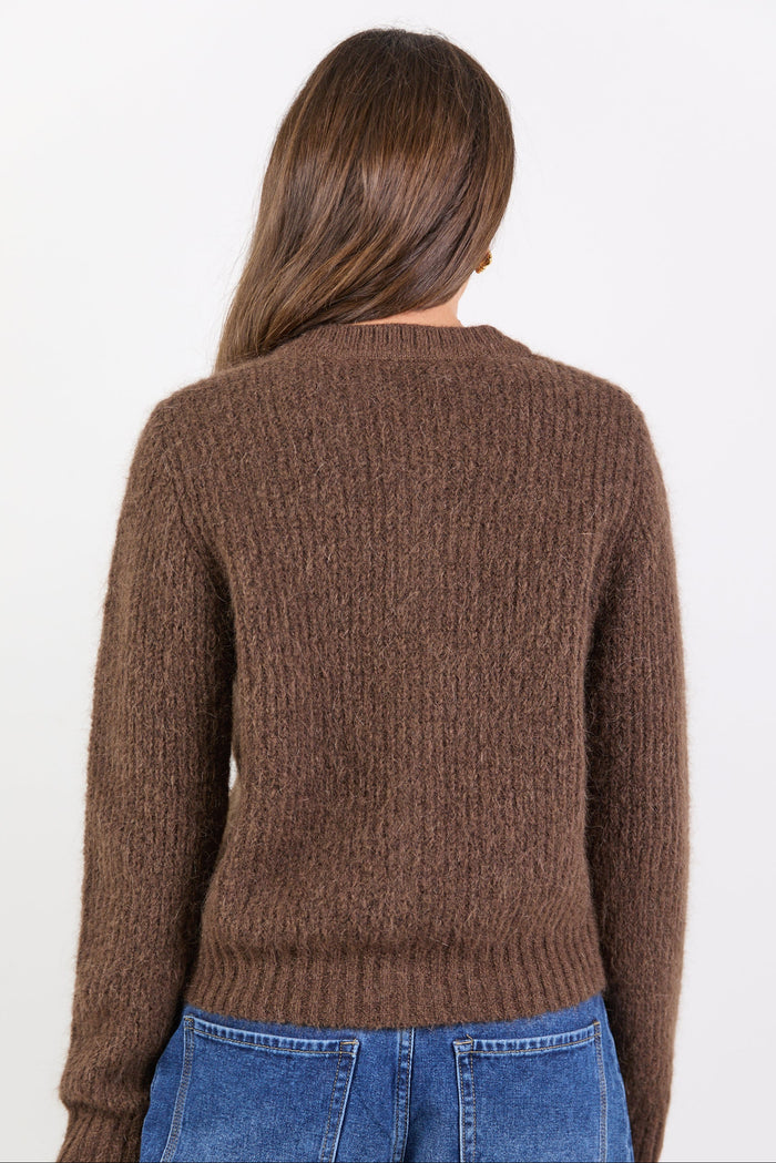 Person wearing a brown sweater and blue jeans on a white background