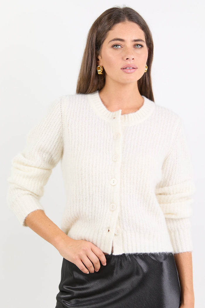 Woman wearing a white ribbed cardigan over a black skirt on a white background