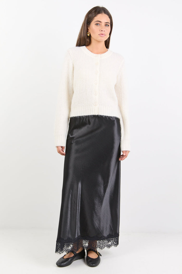 Woman wearing a white top and black skirt with lace details on a white background