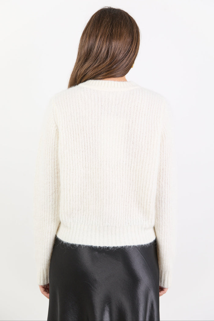 Person wearing a white ribbed sweater and black pants on a plain background