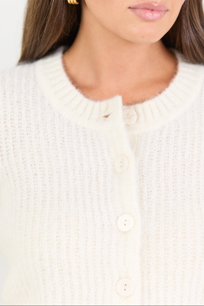 Woman wearing a cream-colored cardigan with a plain background