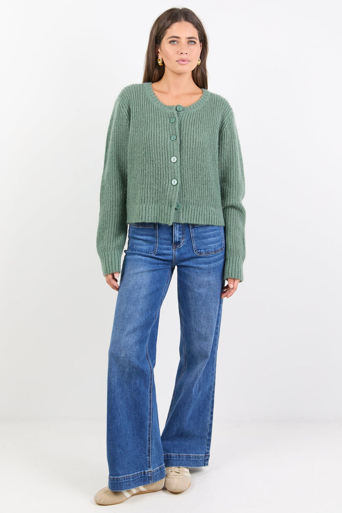 Woman wearing a green cardigan and blue jeans on a white background