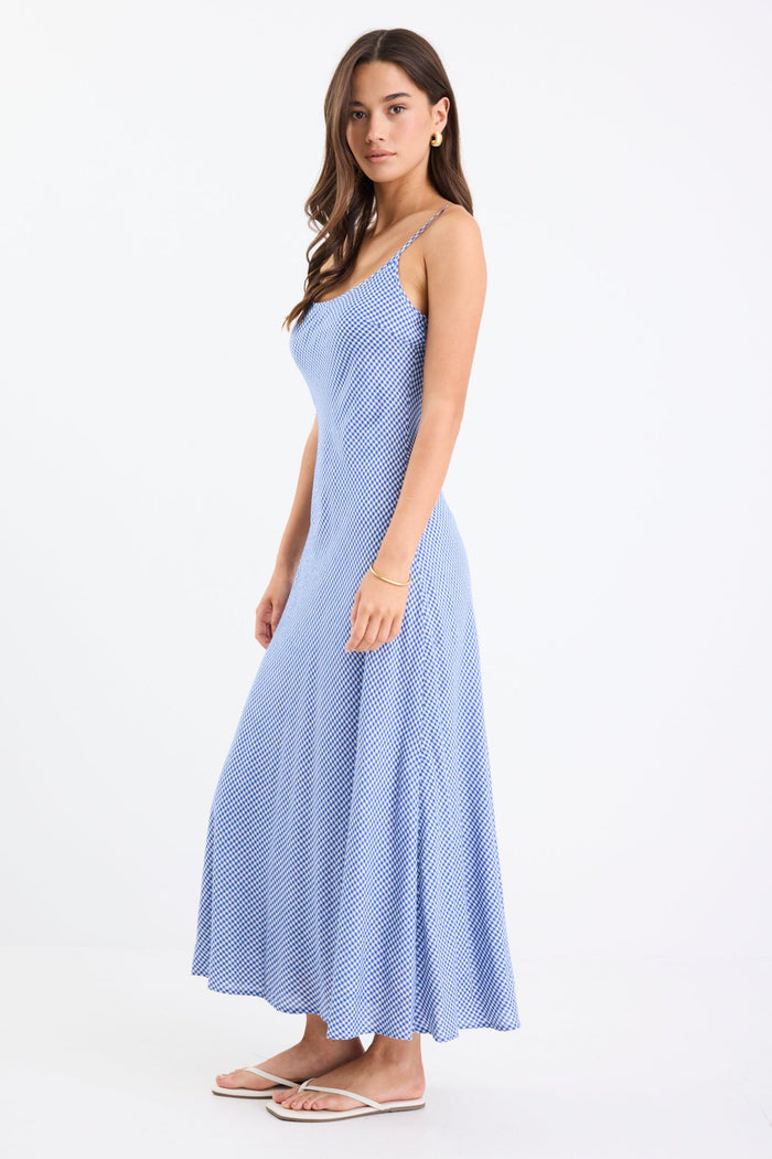 Model wearing a mini gingham strappy slip dress in electric blue, with adjustable straps and a flattering bias cut.