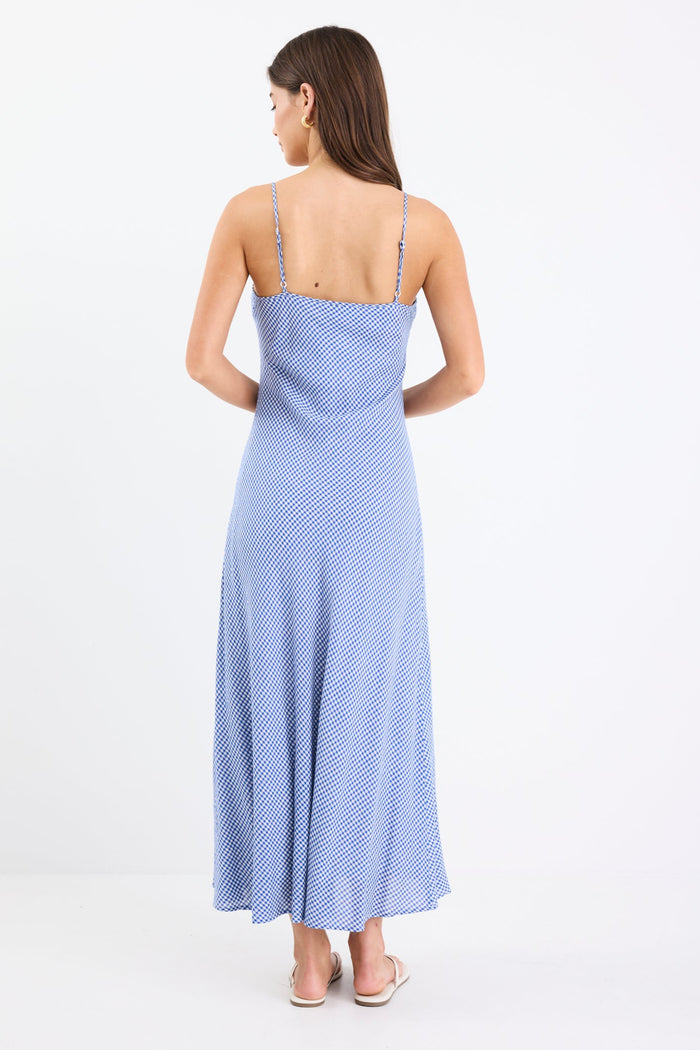 Model wearing a mini gingham strappy slip dress in electric blue, with adjustable straps and a flattering bias cut.