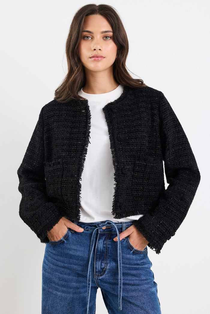 Woman wearing a black textured cardigan over a white shirt and blue jeans on a white background