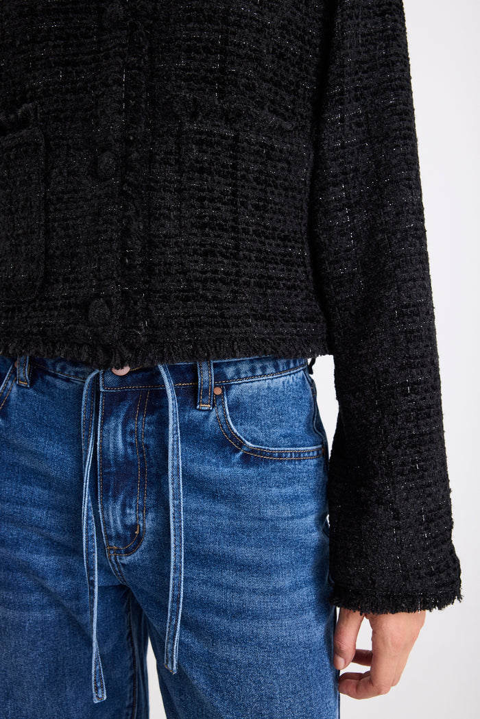 Person wearing a black textured sweater and blue jeans on a white background