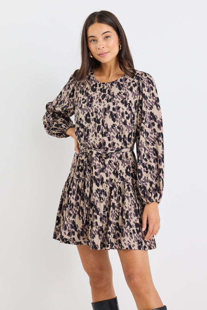 Woman wearing a long-sleeve mini dress with an animal print pattern, belted at the waist with a flared tiered skirt and black boots.