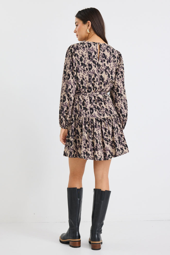 Woman wearing a long-sleeve mini dress with an animal print pattern, belted at the waist with a flared tiered skirt and black boots.