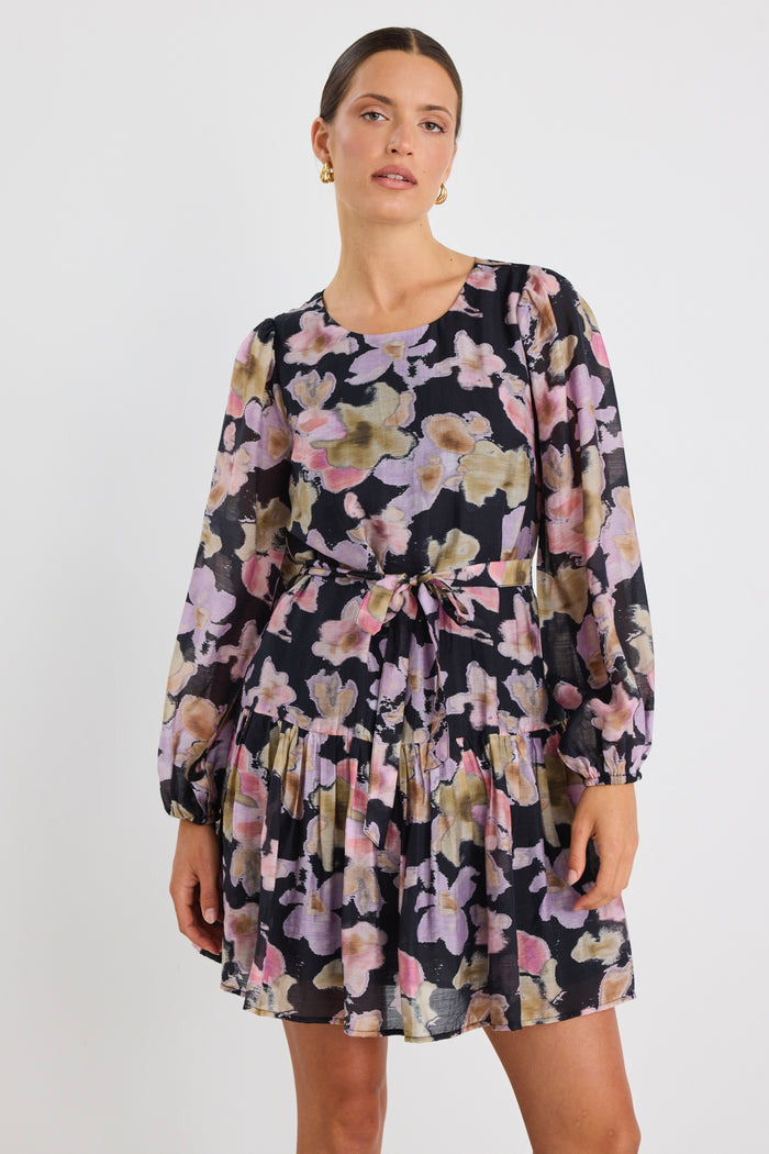 Woman wearing a long-sleeve floral mini dress with a tie waist and tiered skirt, styled with knee-high black boots and sunglasses.