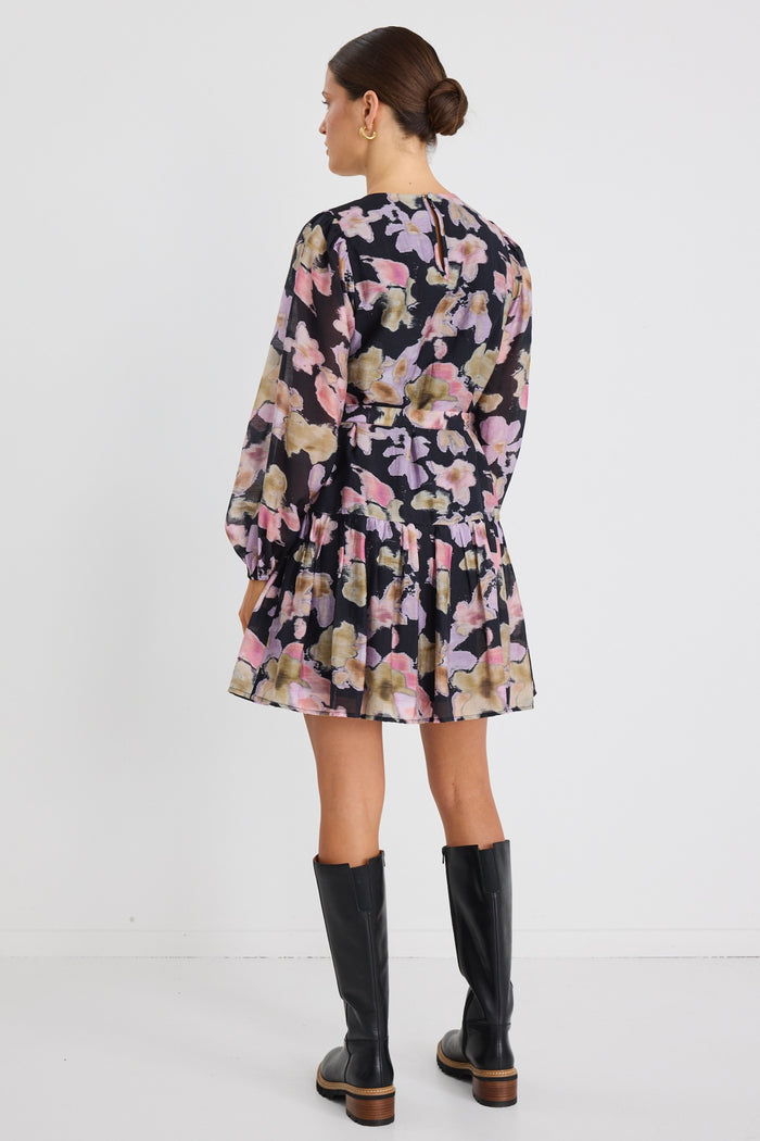 Woman wearing a long-sleeve floral mini dress with a tie waist and tiered skirt, styled with knee-high black boots and sunglasses.