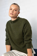 Woman wearing a green sweater sitting on a chair against a white wall
