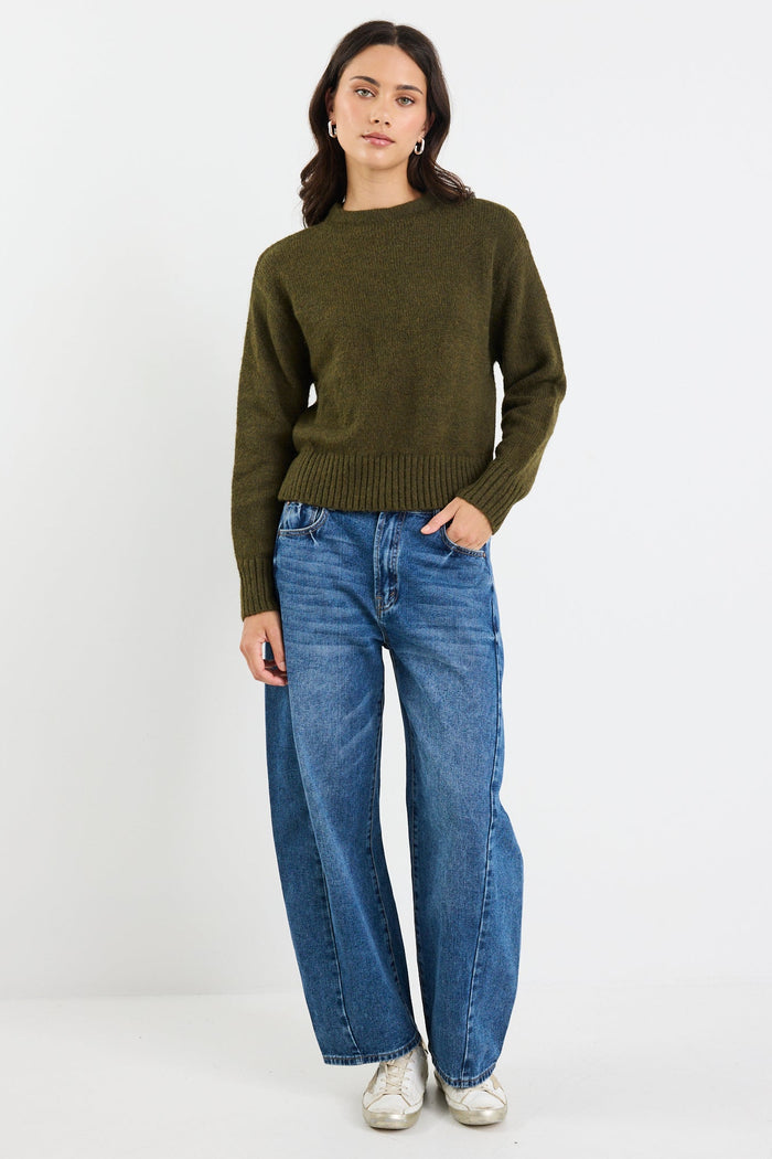 Person wearing a green sweater and blue jeans on a white background