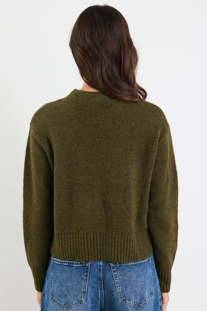 Person wearing a green sweater and blue jeans on a white background